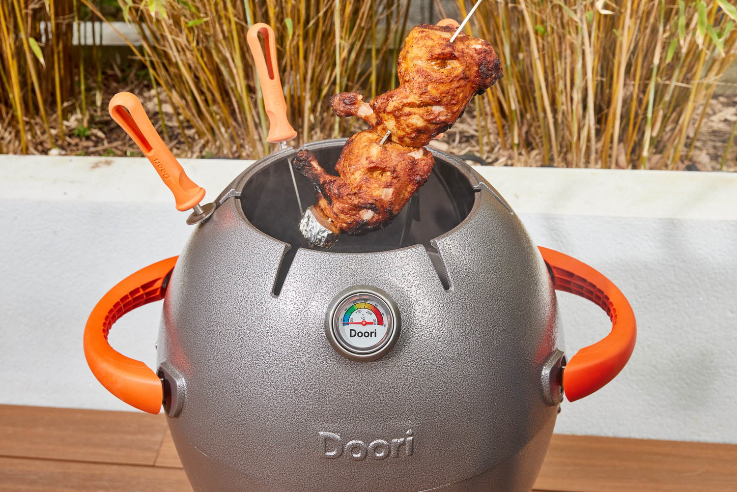 A skewer of chicken being pulled out of the Doori Outdoor Cooker.