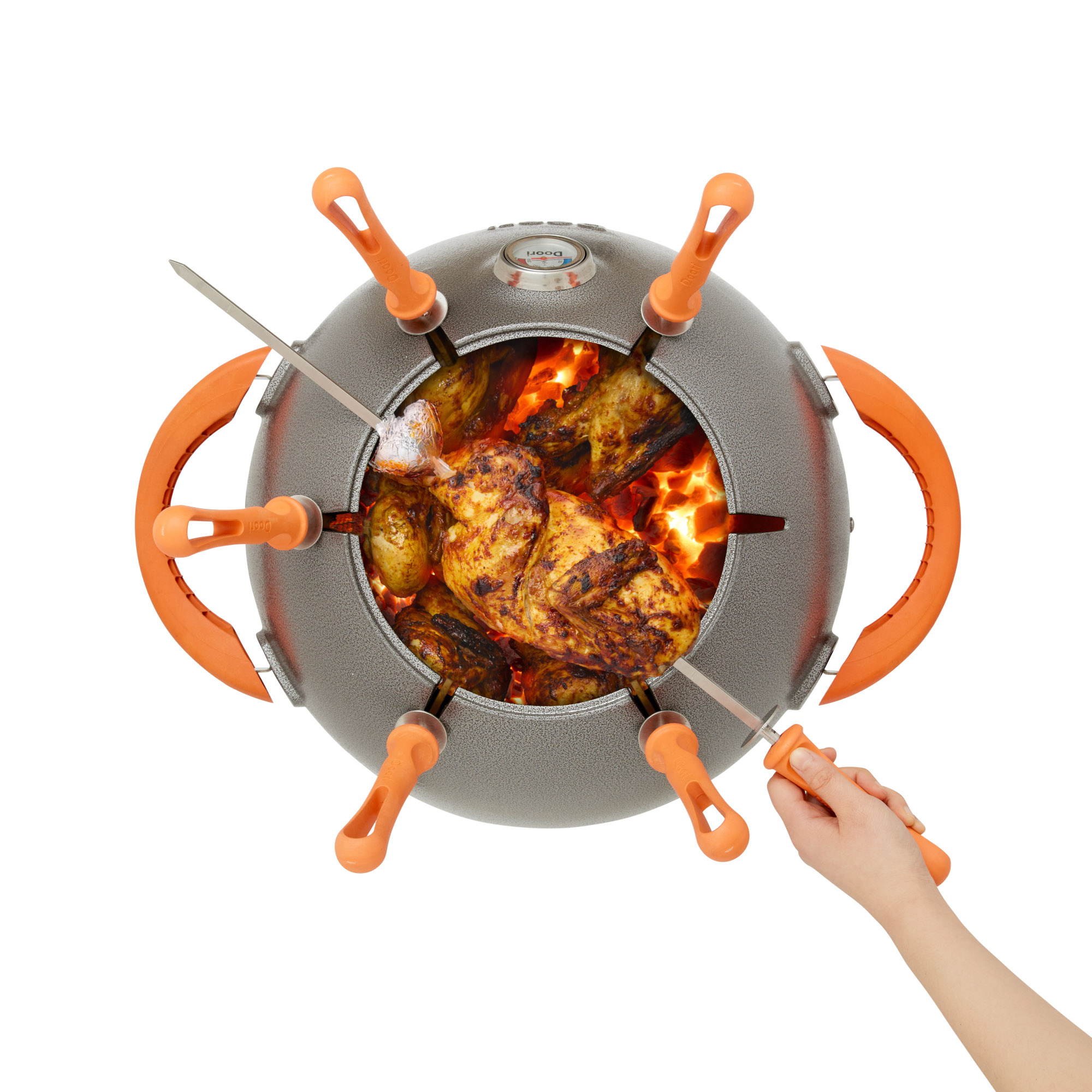 A hand holding a skewer of chicken over an open Doori Outdoor Cooker.